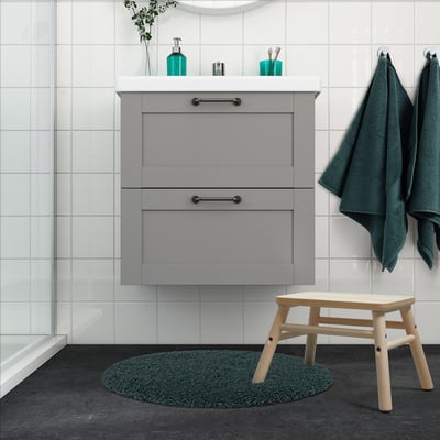 Modern bathroom with ALMTJÄRN grey-turquoise mat, grey cabinet, wooden stool, white tiles, and green towels. Mat small, fitting neatly under cabinet.