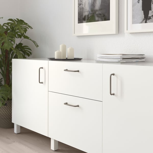 White BAGGANÄS cabinet with metal handles on wood floor, frame, plant.