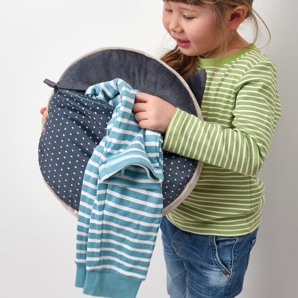 A child holding a round cushion with a secret pocket, designed like a cat, perfect for storing pyjamas.