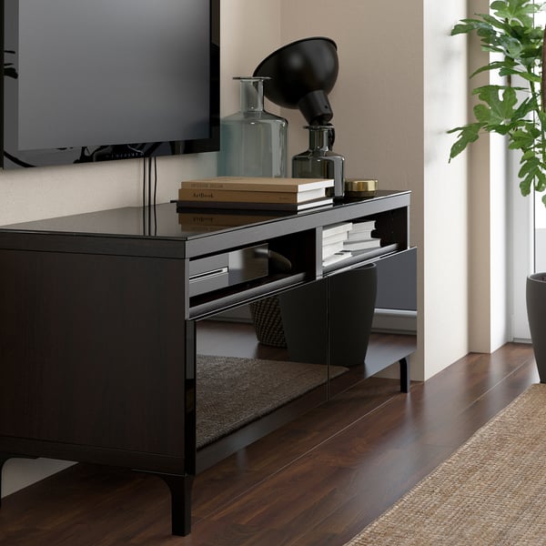 Glass tv stand with books, vases, lamp, tv, plant, rug on wood floors.