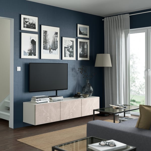 Modern living room with grey walls, marble tv bench, flat-screen tv, black and white photos, glass coffee table, and floor lamp.