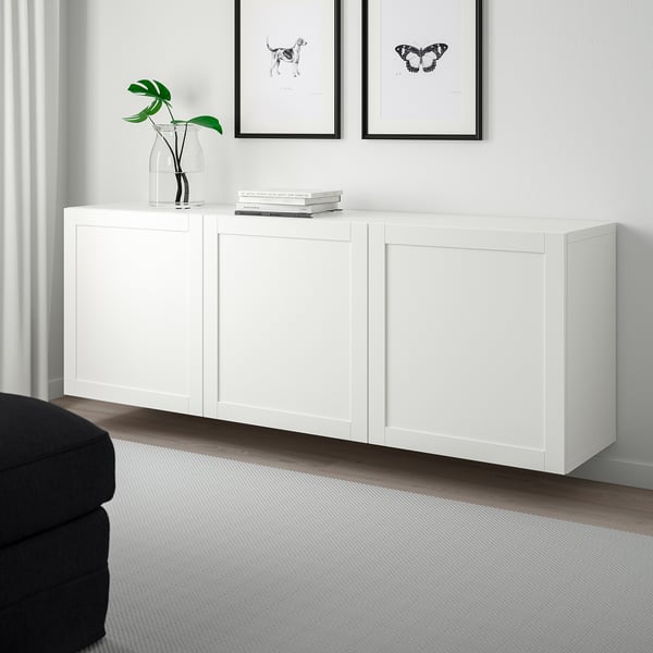 White BESTÅ cabinet with adjustable shelves, soft-close doors, holding vase, books, and black-white pictures, dark grey sofa, light rug below.