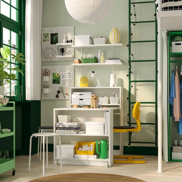 BILLY bookcase with foldable table in organised room. White storage with decor. Extendable workspace, green-yellow scheme.