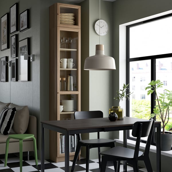 Modern dining area with BILLY tall wooden storage, green wall, black chairs, table, signature lamp, art gallery wall, large window, and plants.