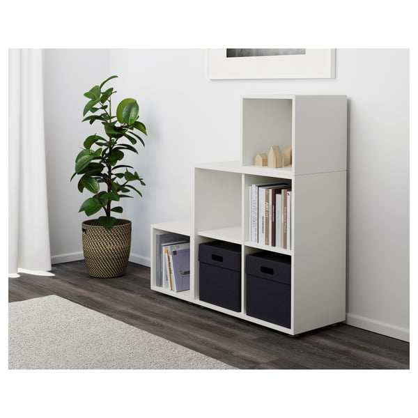 White modular shelf unit EKET, featuring open and storage boxes. Accommodates books and supplied bins. Fixed to wall for stability.