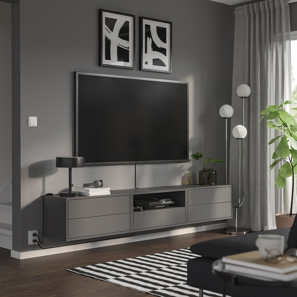 Modern living room with sleek, grey EKET tv unit, flat screen tv, stylish lamps, and plants; minimalist decor.