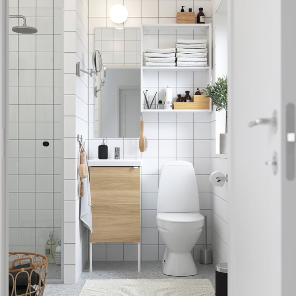 Minimalist bathroom with grey tiles, white fixtures & wood vanity. Towels, plants, & toiletries stored neatly.