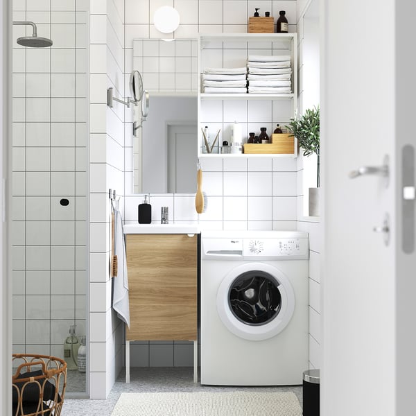 Compact laundry room: washing machine, shelves, mirror, cabinet, shower.