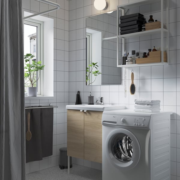 Bathroom with washer, sink, mirror, & shelves holding towels & toiletries. Grey shower curtain left.