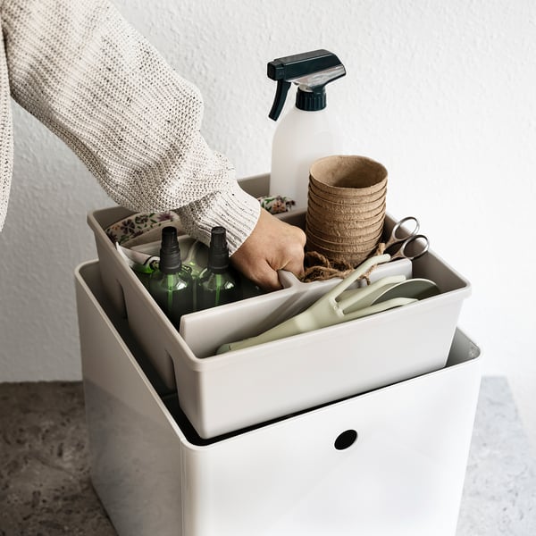 Hand reaches into FÅNGGRÖDA storage insert with various items on white surface.