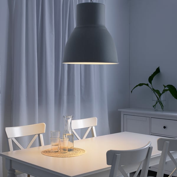 A modern dining room a large HEKTAR pendant lamp casting warm, even light over a white table with glassware, creating a cosy atmosphere for meals.