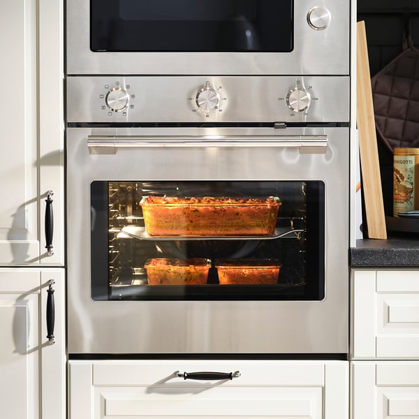 Stainless steel oven with clear glass door, baking two dishes with an item inside, set on middle rack.