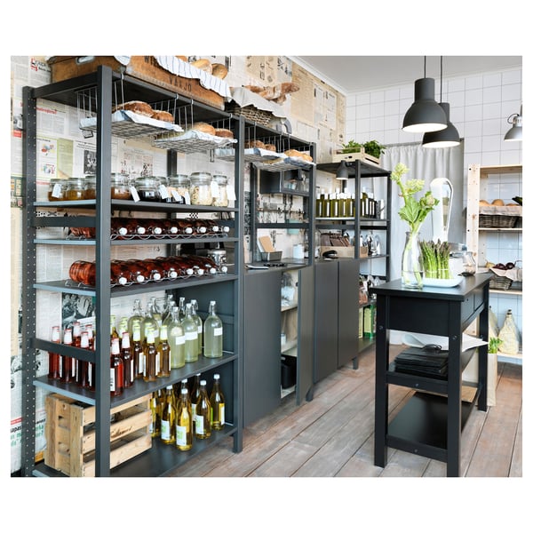 Modern kitchen with black IVAR shelves and table, displaying jars, bottles, crates, and plants.