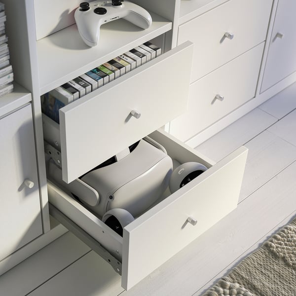 White KALLAX storage unit with open drawers holding gaming controllers, stack of games on top.