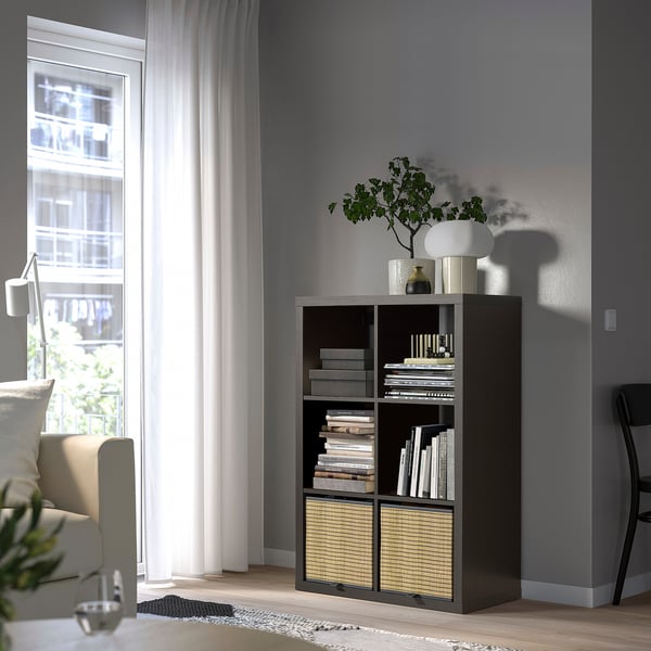 KALLAX bookshelf in grey by window, filled with books and a vase of flowers.