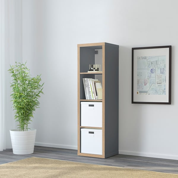 KALLAX shelf in dark grey with light wood trim, holding storage boxes, books, and a plant.