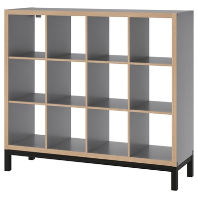 A KALLAX shelf unit in gray with light wood accents and black legs. It has a modular, cube-like design with open compartments.