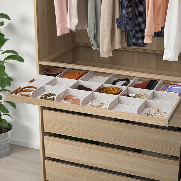Wooden wardrobe drawer with grey organiser trays storing belts, ties, and jewellery.
