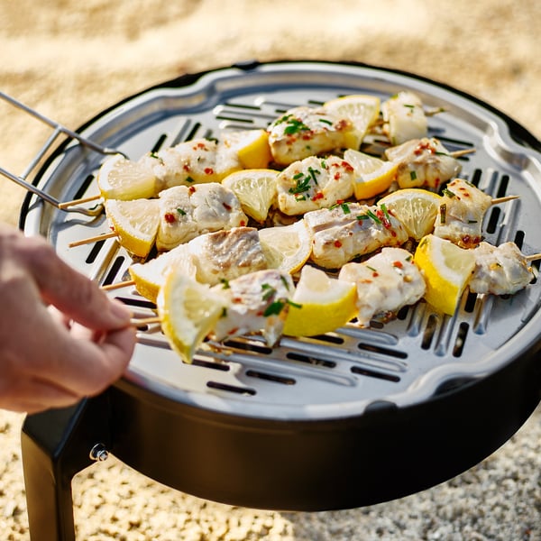 Grilling fish skewers with lemon on portable charcoal grill with vented design for high temps, ideal outdoors.
