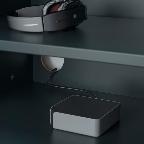 A pair of grey headphones resting on a dark surface, connected to a charging device.