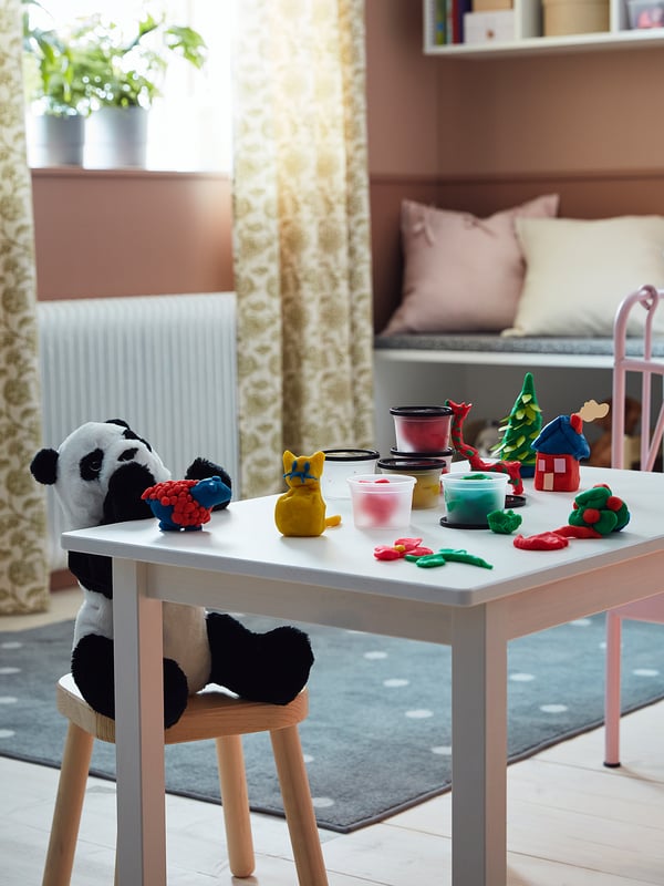 Kids table with colourful MÅLA dough. Panda, cat, and toys. Bright room with curtains.