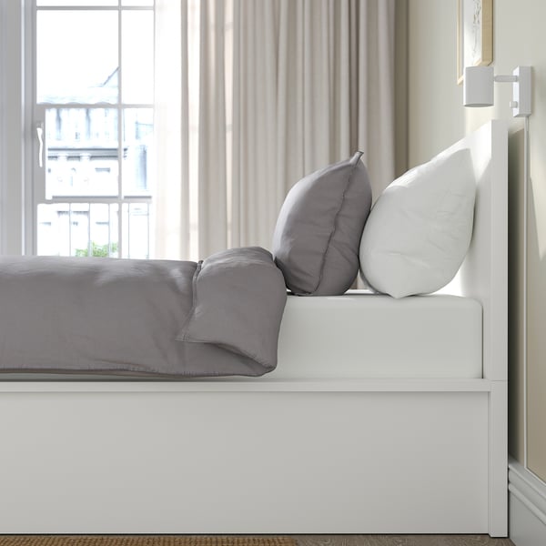 Bed with lift-up base revealing storage. Grey bedding and pillows, headboard against wall.