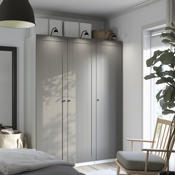 A modern bedroom with a large grey PAX wardrobe, tall and sleek, standing against the wall, flanked by a hanging lamp and a small wooden chair.