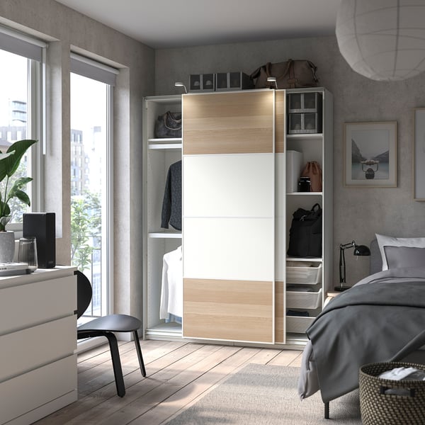 Modern bedroom with white oak PAX, grey chair, bed, side table, city view.