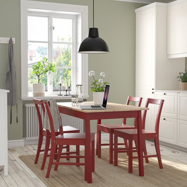 Red PINNTORP dining set with pine table & chairs fits cosy spaces. Tabletop with laptops and flowers, white kitchen cabinets in background.