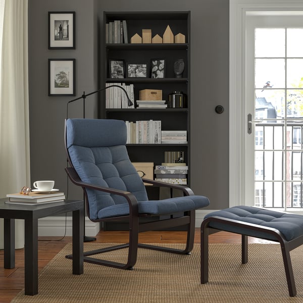 Modern living room: blue poang armchair & footrest, dark wood bookcase, large window, black & white photos.