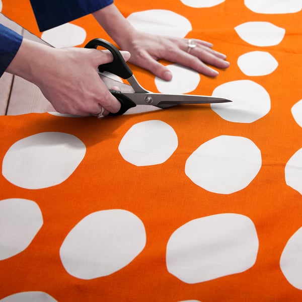 Person holds scissors cutting orange fabric with white polka dots.