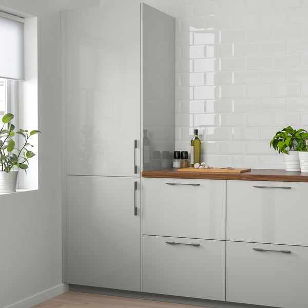 Modern kitchen with glossy RINGHULT cabinets, sleek design, reflecting light, functional counters with items and plants.