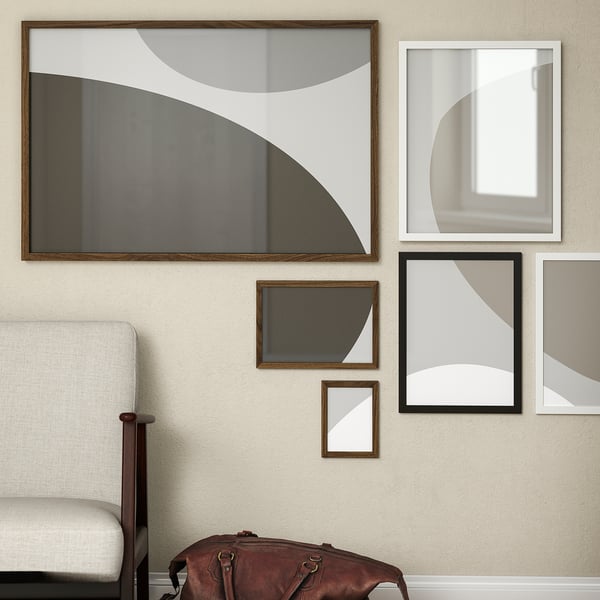 Wall gallery with RÖDALM frames; large abstract frame, smaller frames, beige wall; brown bag, white chair.