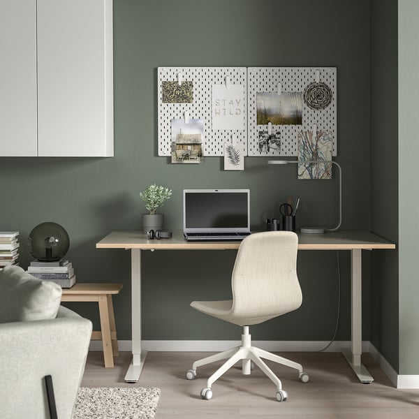 Minimalist home office: green wall, desk, chair, laptop, pegboard.