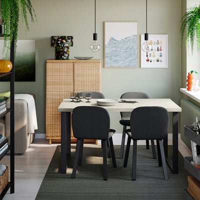 A modern dining room with SKÅLSTA table, grey chairs, white settings, photos, lights, and a green rug. Minimalist and inviting.