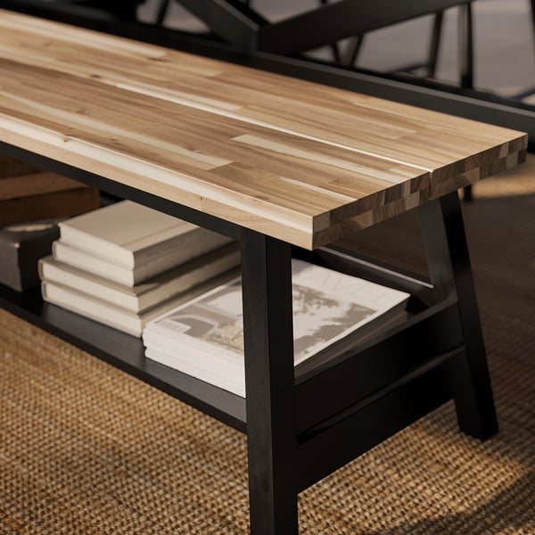 A wooden bench with black metal legs, featuring a lower shelf holding books and a magazine.