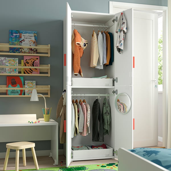 A SMÅSTAD kid’s wardrobe in white, organised with clothes and books, including a cuddly toy; set against a blue wall.
