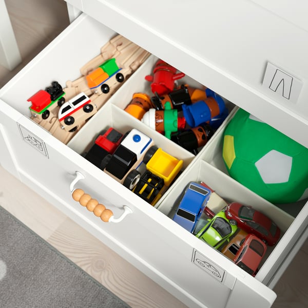 White toy chest with divided drawers holding various colourful toys.