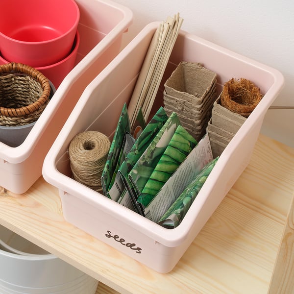 A pink SOCKERBIT storage box holding seeds, twine, and plant pots, labelled seeds on the front.