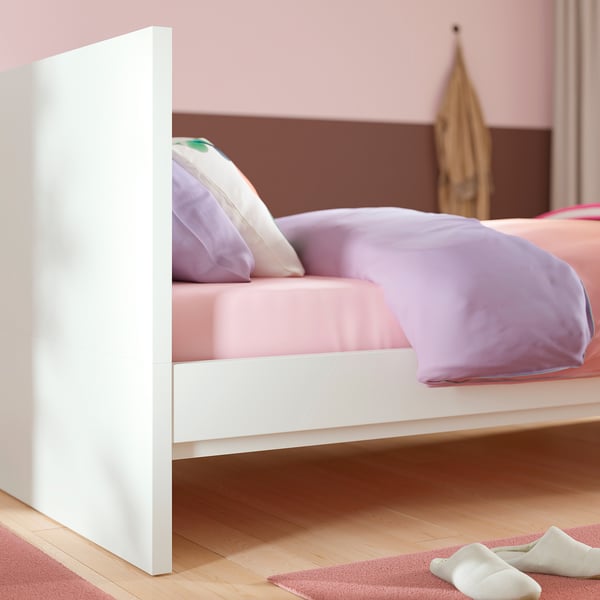 A white modern bed with a high headboard, purple bedding, and slatted base, designed for easy cleaning and optional under-bed storage.