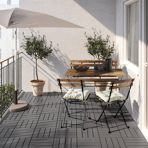 Balcony setup: tarnö wooden bench with metal chairs, table, and olive trees.
