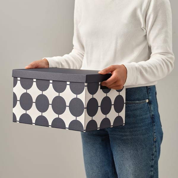 Person holding a TJENA storage box with a geometric pattern. The box has a handle for easy access.