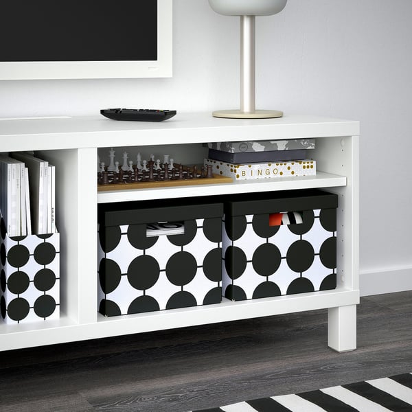 White tv stand with storage shelves. Includes black and white patterned boxes, containing games like chess and bingo, books, and other items.