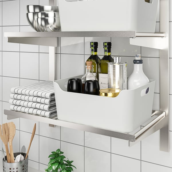 A kitchen shelf with organiser, storing bottles, cups, towels, and utensils neatly.