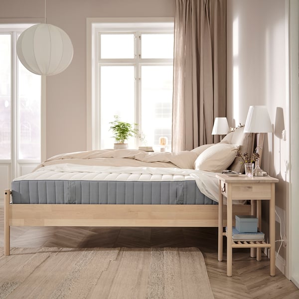 Beige-themed bedroom with VALEVÅG bed, white bedspread, bedside table, lamp, hanging light, and large window with sheer curtains.