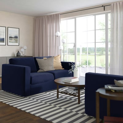 Blue VIMLE sofa, modern minimalist design, large windows, striped rug, wooden tables, cosy and spacious living room.