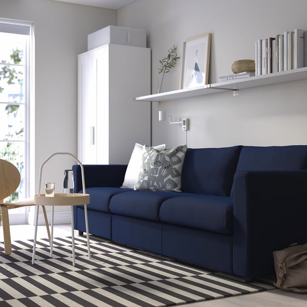 Modern living room with navy sofa, striped rug, white cabinet, books, and plants.
