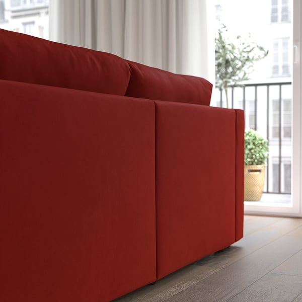 Bright red sofa with smooth fabric, plush cushions, and an adjacent window with a potted plant.
