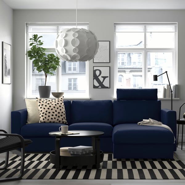 Cosy living room with blue VIMLE sectional sofa, large window, pendant lamp, black-and-white rug, and plants.