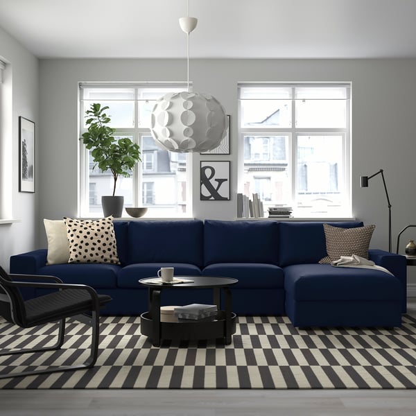 Modern living room with large blue VIMLE sectional sofa, stripe rug, black coffee table, unique pendant light, and city view.